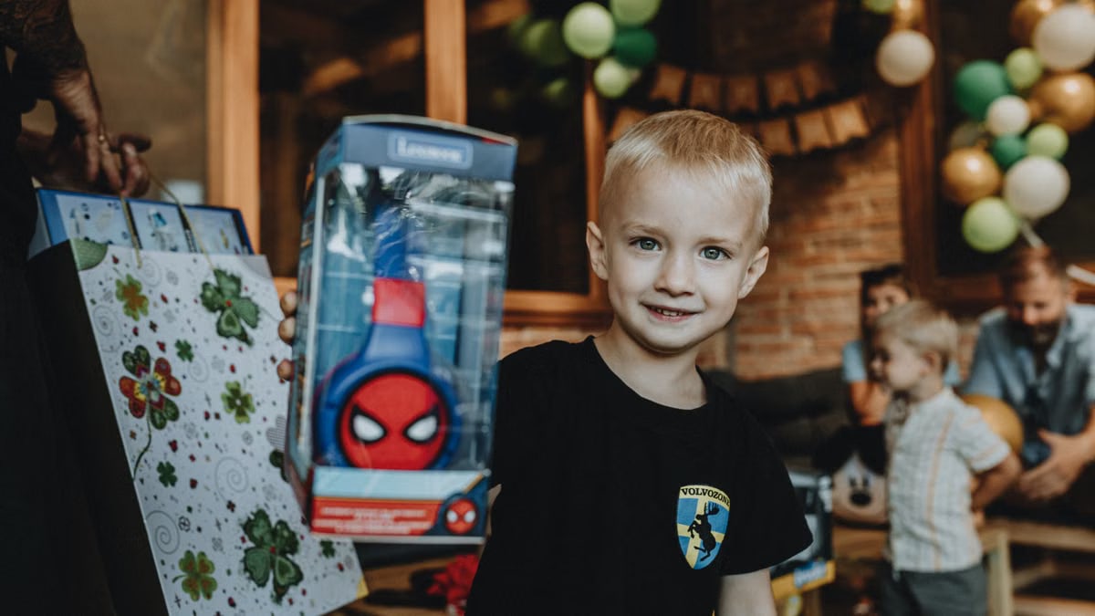 Smiling child holding a superhero-themed gift at a birthday party.